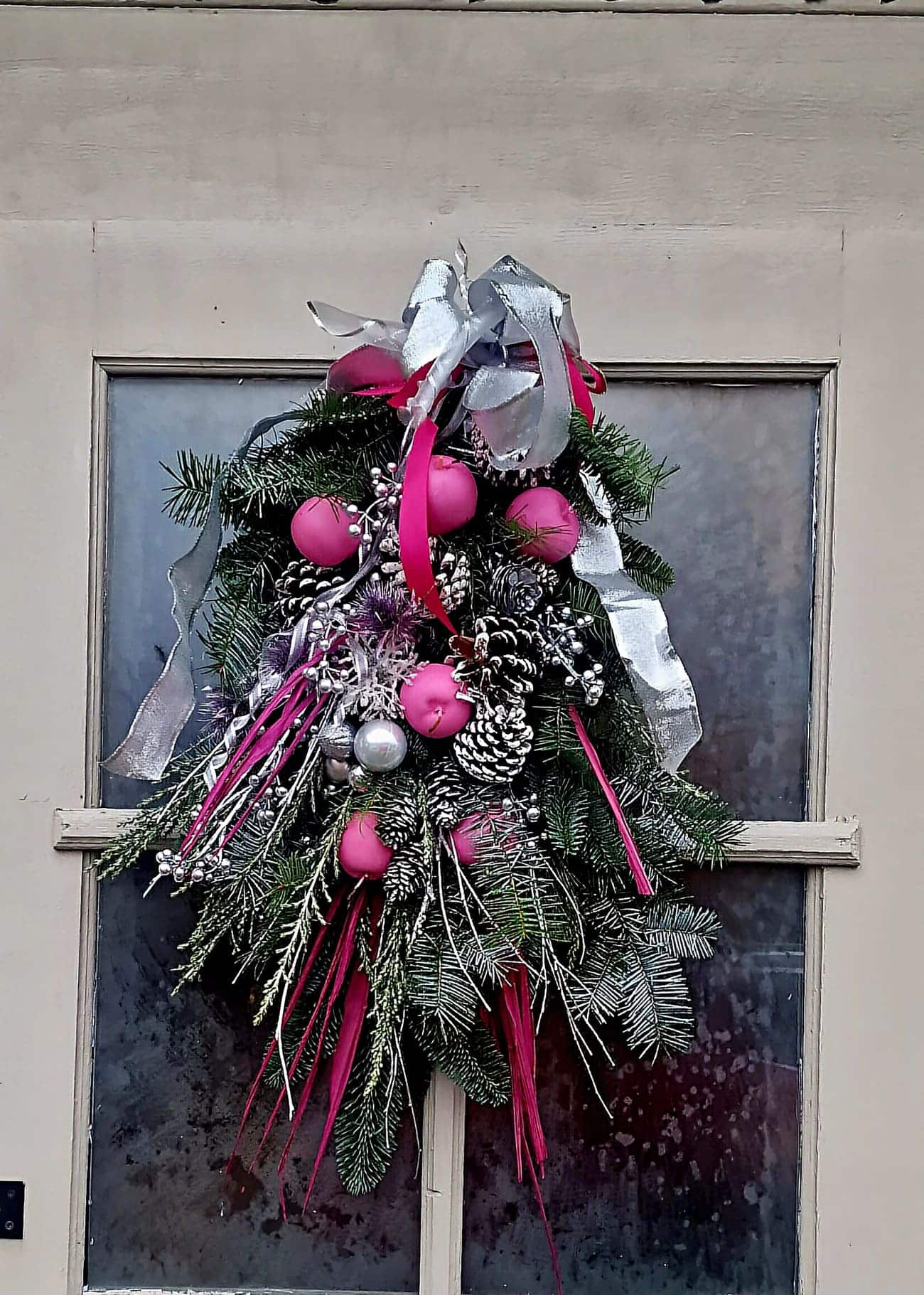 Pink and silver Christmas door swag with evergreens and frosted pine cones.